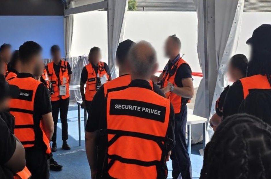 Security officers in orange vests at a briefing before an event, faces blurred